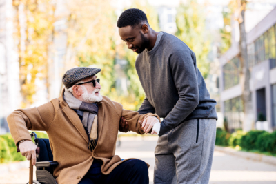 young african american caregiver helping senior disabled man